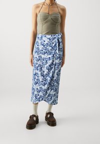 Tanktop i bomullsblandning i olivgrön, tillsammans med en blå mönstrad omslagskjol, stylad med bruna platåskor och beige strumpor.