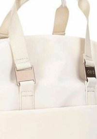 Witte draagtas met beige stoffen banden en metalen beslag. Heeft een gladde textuur en een minimalistisch ontwerp met een eenvoudige sluiting.