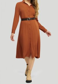 Rostfärgad skjortklänning med långa ärmar, knäppning fram, belagd midja och lätt A-linjeform, matchad med beige ankelskor.