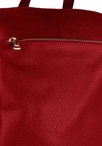 Rood leren handtas met een gestructureerd oppervlak, een ritsvak met gouden hardware en stevige handvatten.