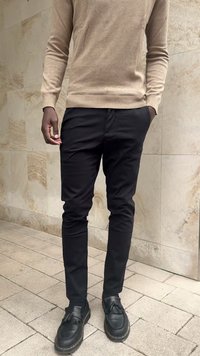 Beige Langarmpullover, schwarze Slim-Fit-Hose, schwarze Loafers mit Quasten. Die Materialien scheinen weich und mit glatten Texturen zu sein.