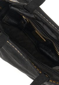 Interno di una borsa a tracolla in pelle nera caratterizzato da una consistenza liscia, zip dorata e dettagli metallici, con bordo cucito e design spazioso.