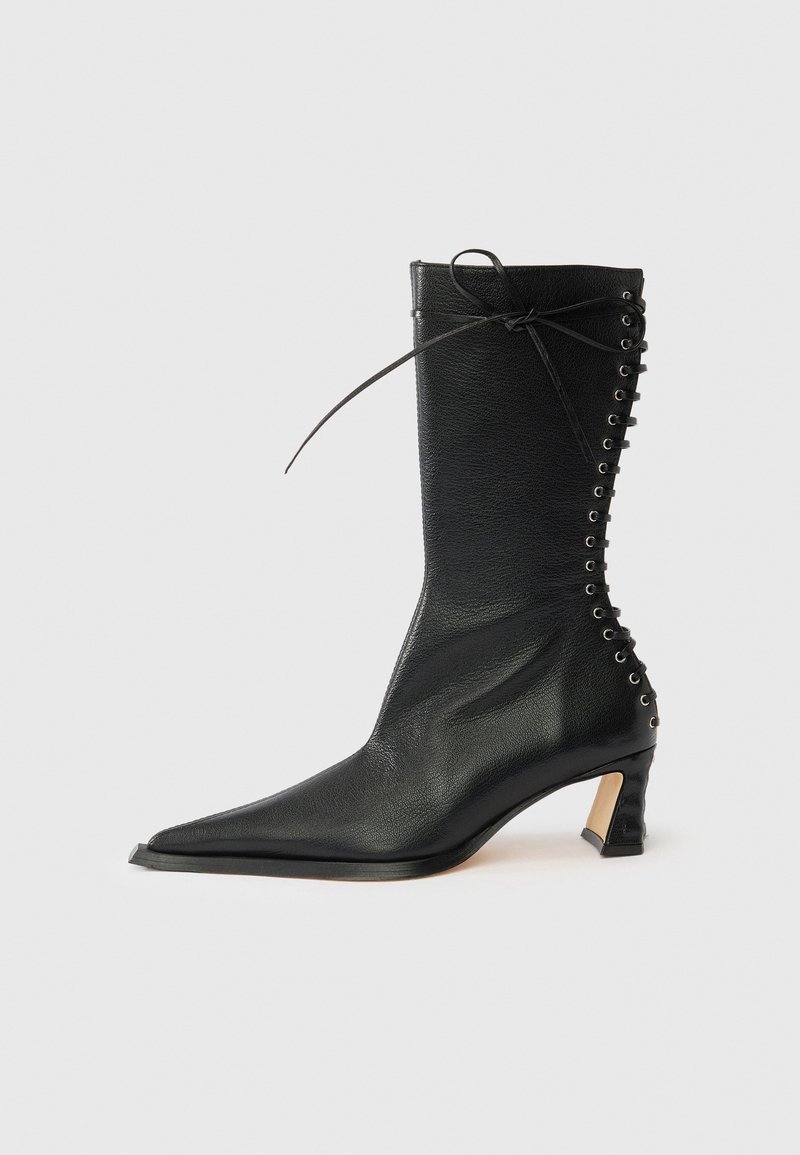 Μαύρο δερμάτινο μποτάκι αστραγάλου με μυτερή μύτη, λεπτό τακούνι, δέσιμο στο πίσω μέρος και μεταλλικά περντήματα. Λείο υλικό με κομψό σχέδιο.