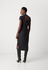 Black, knee-length dress with a round back cutout and short sleeves; features side slits and a fitted design. Worn with knee-high black boots.