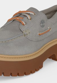 Chaussure bateau en daim gris avec lacets en cuir orange, détails cousus, logo arbre Timberland et semelle épaisse en caoutchouc marron à crampons.
