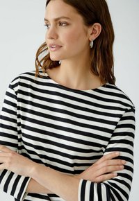 Schwarz-weiß gestreiftes Shirt mit weitem Ausschnitt und Dreiviertelärmeln, aus weichem Stoff, präsentiert an einem Modell mit verschränkten Armen.