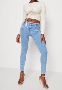 Jeans ajustados de color azul claro con una cintura alta, costuras en contraste y un diseño de pierna ajustada. Combinados con una blusa de manga larga beige.