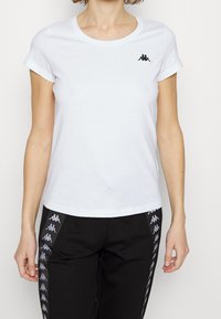 Bílý tričko s krátkým rukávem vyrobené z bavlny. Na levém prsu se nachází černé logo. Hladký povrch, klasický kulatý výstřih.