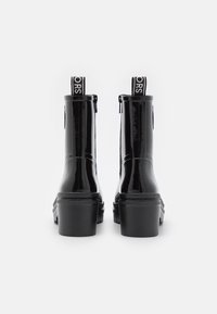 Bottes à cheville en cuir verni noir avec un talon carré, fermeture à glissière et languettes de traction présentant un logo contrasté à l'arrière.