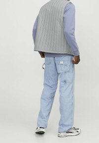 Grå vadderad väst över en ljusblå långärmad skjorta, i kombination med ljusblå cargojeans med fickor och en liten etikett.