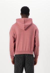 Sweat à capuche surdimensionné rose avec une texture douce, doté d'une capuche et d'accents en clous argentés sur les manches. Taille et poignets côtelés.