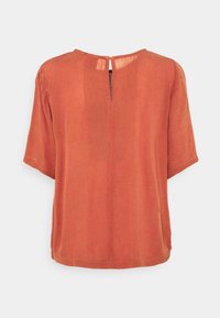 Blouse à manches courtes couleur rouille, coupe droite, texture douce, avec un petit détail en forme d'œillet au dos du col.