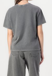 Šedé oversized tričko vyrobené z jemné, vybledlé bavlny, s krátkými rukávy, kulatým výstřihem a uvolněným střihem, spárované se šedými kalhotami ve stejném odstínu.
