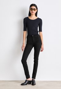 Sorte høyhalsede jeans med slim fit, kombinert med en kortermet marineblå topp og svarte høye tresko. Mykt stoff, tettsittende silhuett.