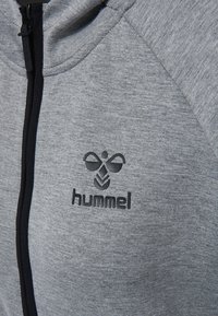 Sudadera con cremallera en gris, hecha de tejido texturizado. Cuenta con cremallera y costuras en negro. Logotipo "hummel" en relieve destacado en el lado izquierdo del pecho.