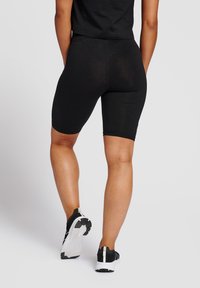 Zwarte fietsbroekjes van rekbaar materiaal, passend, met een gladde textuur, eindigend boven de knie, gedragen met zwart-witte sportschoenen.