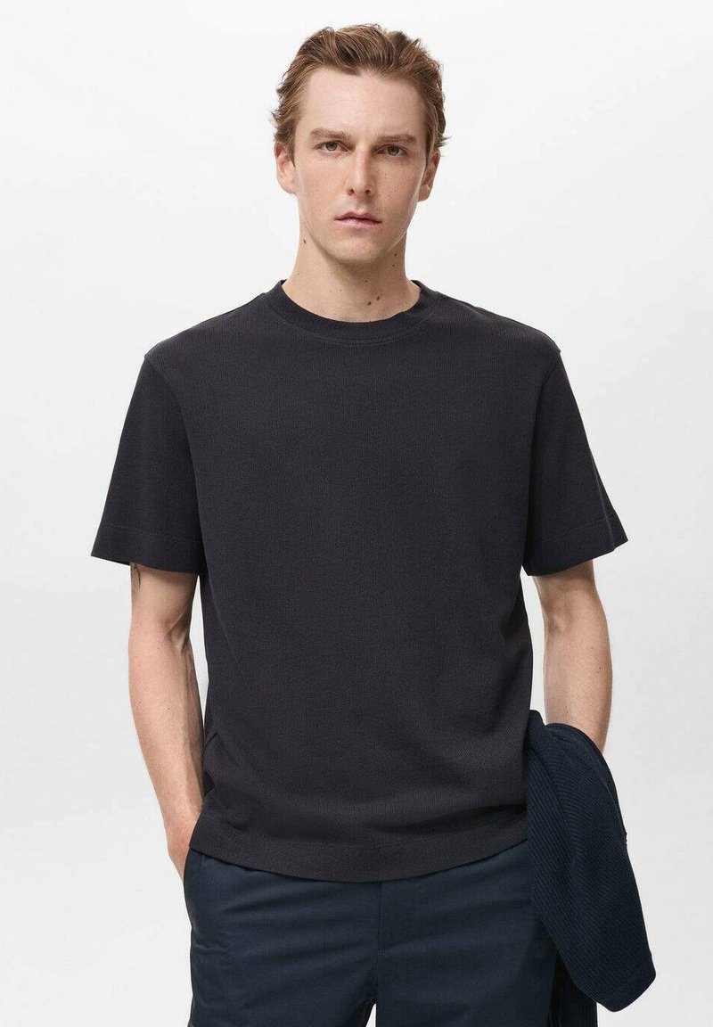 Tricou cu mânecă scurtă de culoare gri închis, cu decolteu rotund, având un material texturat și o croială lejeră. Purtați cu pantaloni închiși la culoare.