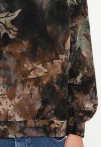 Fleece sweatshirt met een patroon van bruin en groene bladeren, zachte textuur en een boordenzoom, met een casual pasvorm die zichtbaar is rond de taille.