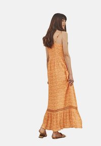 Vestido maxi de tela naranja con estampado de olas, tirantes finos ajustables, corsé fruncido, dobladillo con volantes en capas y un corte relajado.