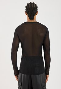 Schwarzes Langarmshirt aus durchsichtigen Material, mit rundem Halsausschnitt und lockerer Passform. Der Rücken zeigt eine glatte Textur und klare Linien.
