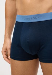 Tumši zili kokvilnas bokseršortus ar gaiši zilu elastīgu jostu, uz kuras ir iegravēts "SCHIESSER" logotips. Mīksta tekstūra, pieguļošs dizains.