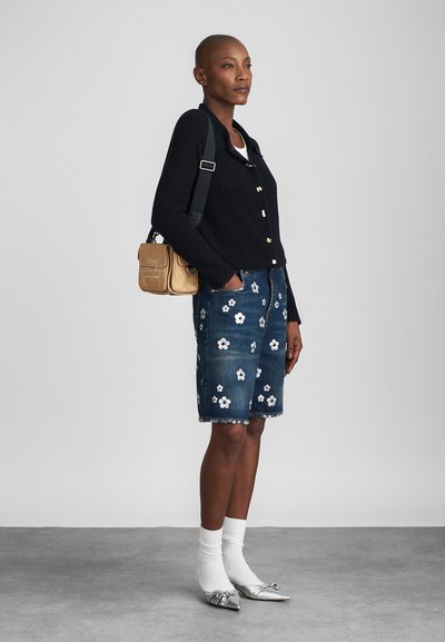 Schwarzer Strickcardigan mit Knopfdetails, Jeansshorts mit weißem Blumenstickereien, silberne Ballerinas und weiße Socken. Inklusive Umhängetasche.