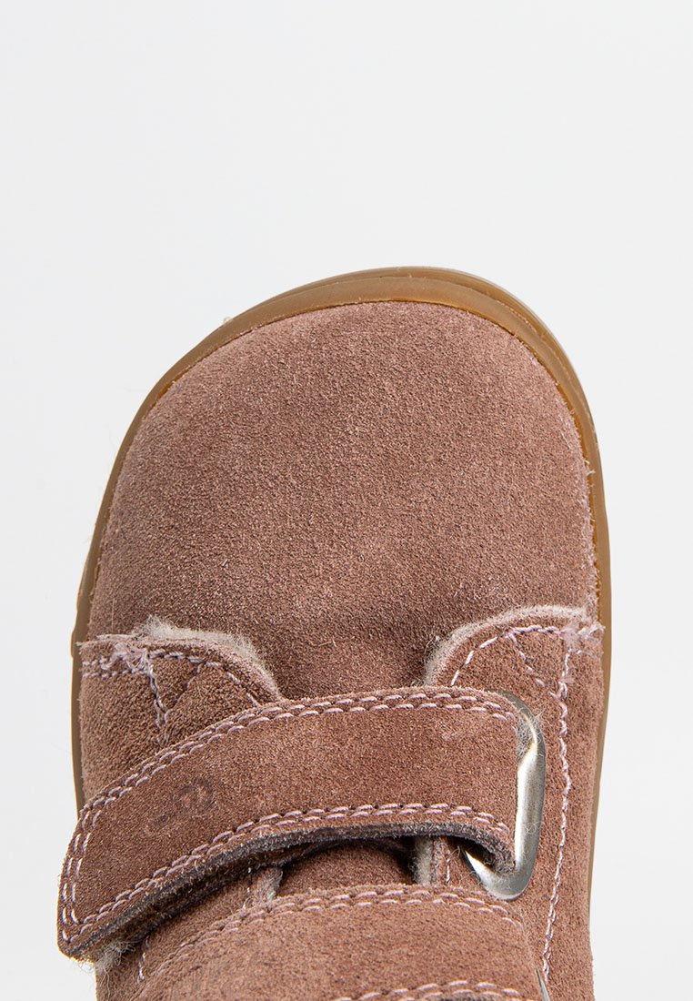 Chaussure en suède marron avec un bout arrondi, une sangle Velcro et une semelle en caoutchouc. Présente des accents de coutures et un détail de boucle en métal lisse.
