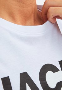 White cotton t-shirt with a round neckline, featuring a large black print. The fabric appears smooth and lightweight.