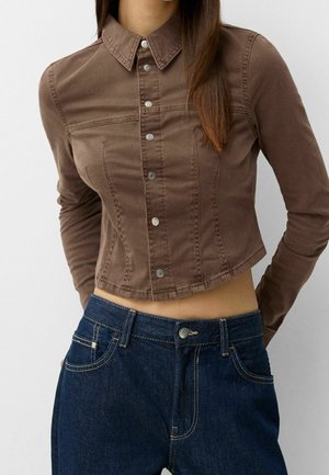 Brun cropped skjorte med knapper og lange ærmer, med krave og sølvfarvede trykknapper. Kombineres med mørkeblå denimjeans.