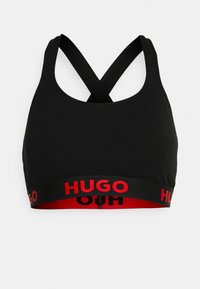 Sutiã desportivo preto com alças cruzadas, apresentando uma faixa elástica em vermelho e preto com o logótipo "HUGO" em destaque.
