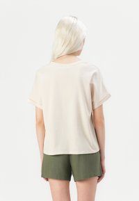 Beige t-skjorte med korte ermer laget av myk bomull, med rund hals og avslappet passform, sammen med grønne shorts.