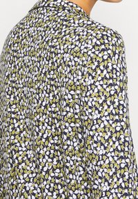 Blusa floreale con sfondo blu scuro e piccoli motivi floreali bianchi e verdi, realizzata in tessuto leggero con una vestibilità morbida.