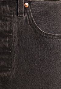 Donkerdenim spijkerbroek met een gladde textuur, met een zichtbare zak en een koperkleurige knoopdetail bij de taille-band.