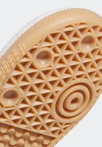 Gummisohle mit einem strukturierten Muster aus Dreiecken und Kreisen; beige Farbe mit einer weißen Kante; glatte und flexible Oberfläche.