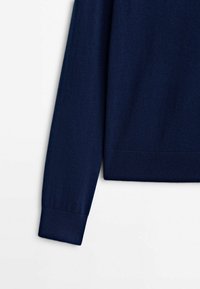 Manche et ourlet inférieur d'un pull en maille bleu marine à manches longues avec poignets et taille côtelés sur fond blanc.