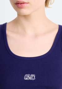 Temno moder rebrast majica brez rokavov z okroglo ovratnikom in belim vezenim logotipom "OBEY" na prednjem delu. Mehka tkanina z oprijetim dizajnom.