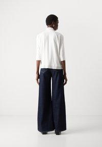 Witte blouse met een hoge kraag en driekwartmouwen, gecombineerd met breedvallende donkerblauwe denim broek. Eenvoudige naden en geen zichtbare patronen.