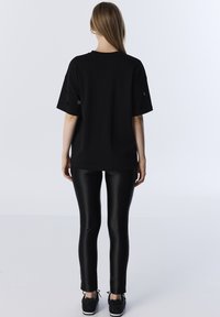 Czarny oversize t-shirt z krótkimi rękawami, gładki materiał i okrągłe wycięcia; w połączeniu z błyszczącymi czarnymi legginsami i teksturowanymi czarnymi sneakersami.