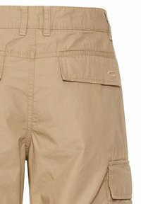 Beige cargo bukser med baglomme-detaljer, lavet af letvægtsstof, med synlige syede sømme og en let krøllet tekstur.