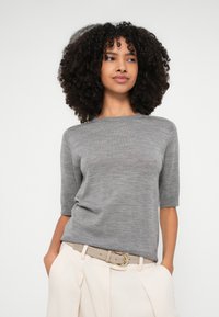 Halli lühikeste varrukatega kudumõeke ümmarguse kaelusega. Sile tekstuur, liibuv stiil, kantud kreemikõrgusega pükstega ja vööga.