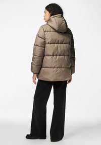 Giacca a vento in marrone caldo, con cappuccio, design trapuntato e polsini elasticizzati. Abbinata a pantaloni larghi neri e stivali chunky.