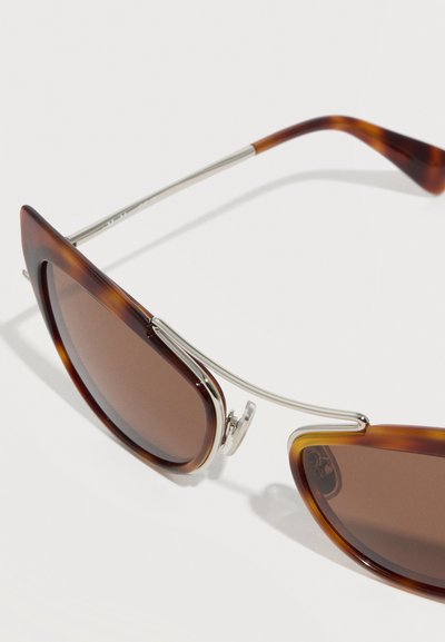 Γυαλιά ηλίου με σχήμα cat-eye, καφέ φακούς με χρωματισμό και σκελετό από οξική τορταλέτα, με λεπτούς ασημένιους μεταλλικούς βραχίονες και ρυθμιζόμενα μαξιλαράκια στη μύτη.