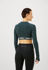 Ciemnozielony, długi top w stylu crop z szarym paskiem "PRO NIKE". Połączony z czarnymi legginsami z wysokim stanem z małym logo z tyłu.