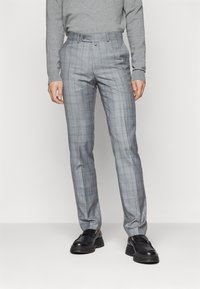 Pantaloni a quadri grigi realizzati in tessuto intrecciato, con taglio dritto, passanti per cintura e tasche laterali. Abbinati a scarpe nere.