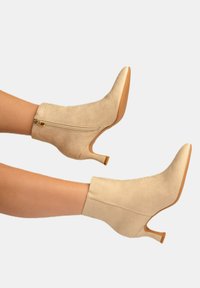 Botas de tobillo de ante beige con punta afilada, cierre de cremallera y un tacón de 3 pulgadas que cuenta con una suela texturada.