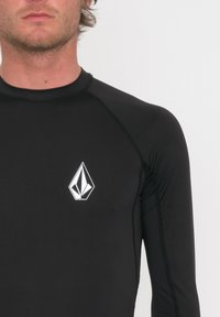 Czarna rash guard z długim rękawem wykonana z elastycznego materiału, z białym logo w kształcie diamentu na lewym piersi. Gładka faktura, dopasowany krój.