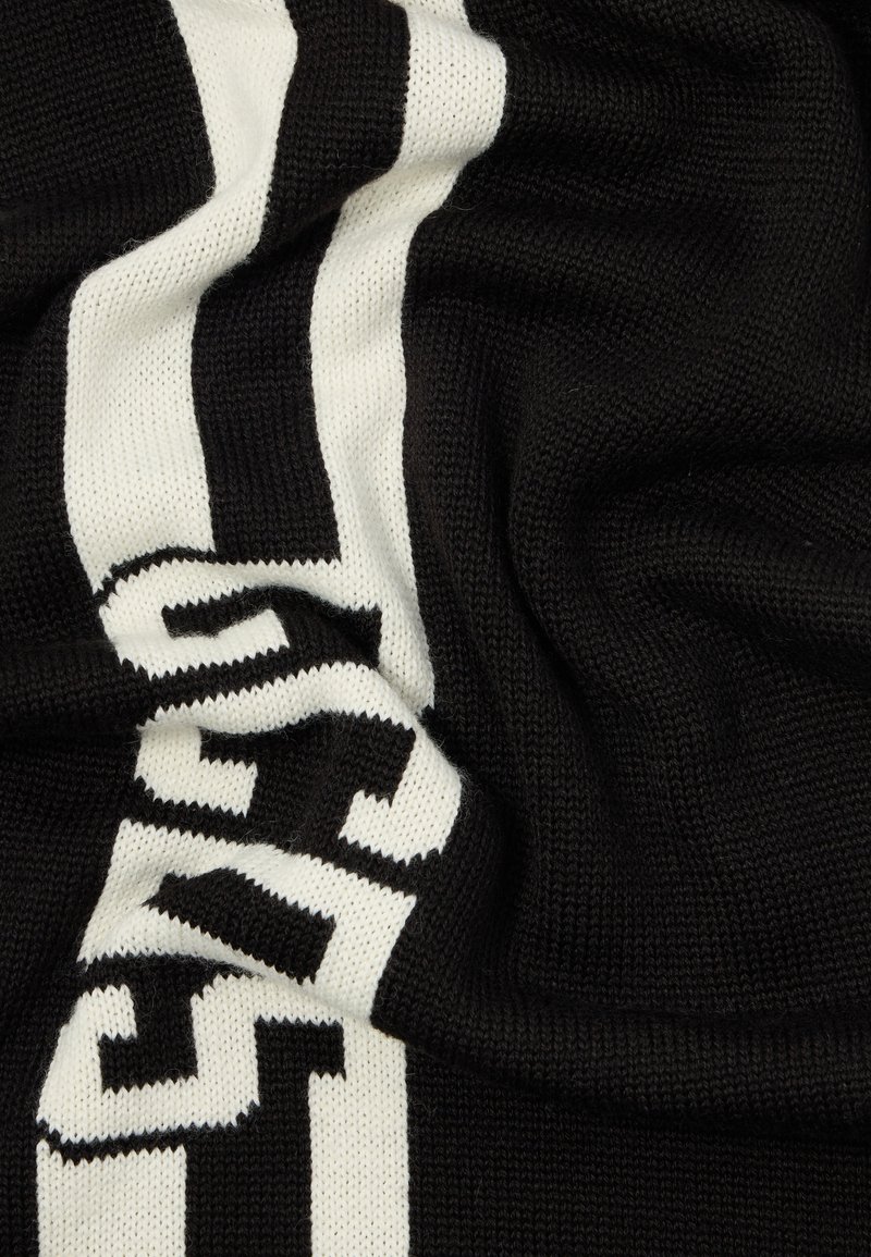 Strickdecke mit einem schwarzen Hintergrund und weißen sowie elfenbeinfarbenen horizontalen Streifen, auf der kühner Text in Schwarz erscheint. Strukturmaterial, das weich ist.