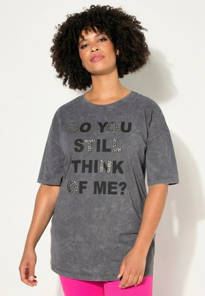 T-shirt gris surdimensionné avec des manches courtes retroussées et un col rond, orné de texte noir décoré de strass : "PENSES-TU ENCORE À MOI ?"