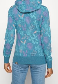 Sudadera color turquesa con patrones botánicos en rosa y azul claro. Con capucha ajustable y puños y dobladillo de canalé.