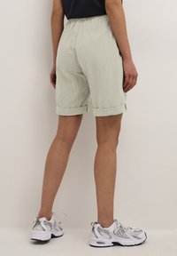 Hellgrüne Leinen-Shorts mit umgeschlagenem Saum, elastischem Bund und strukturierter Stoffqualität, kombiniert mit weißen und silbernen Sportschuhen.